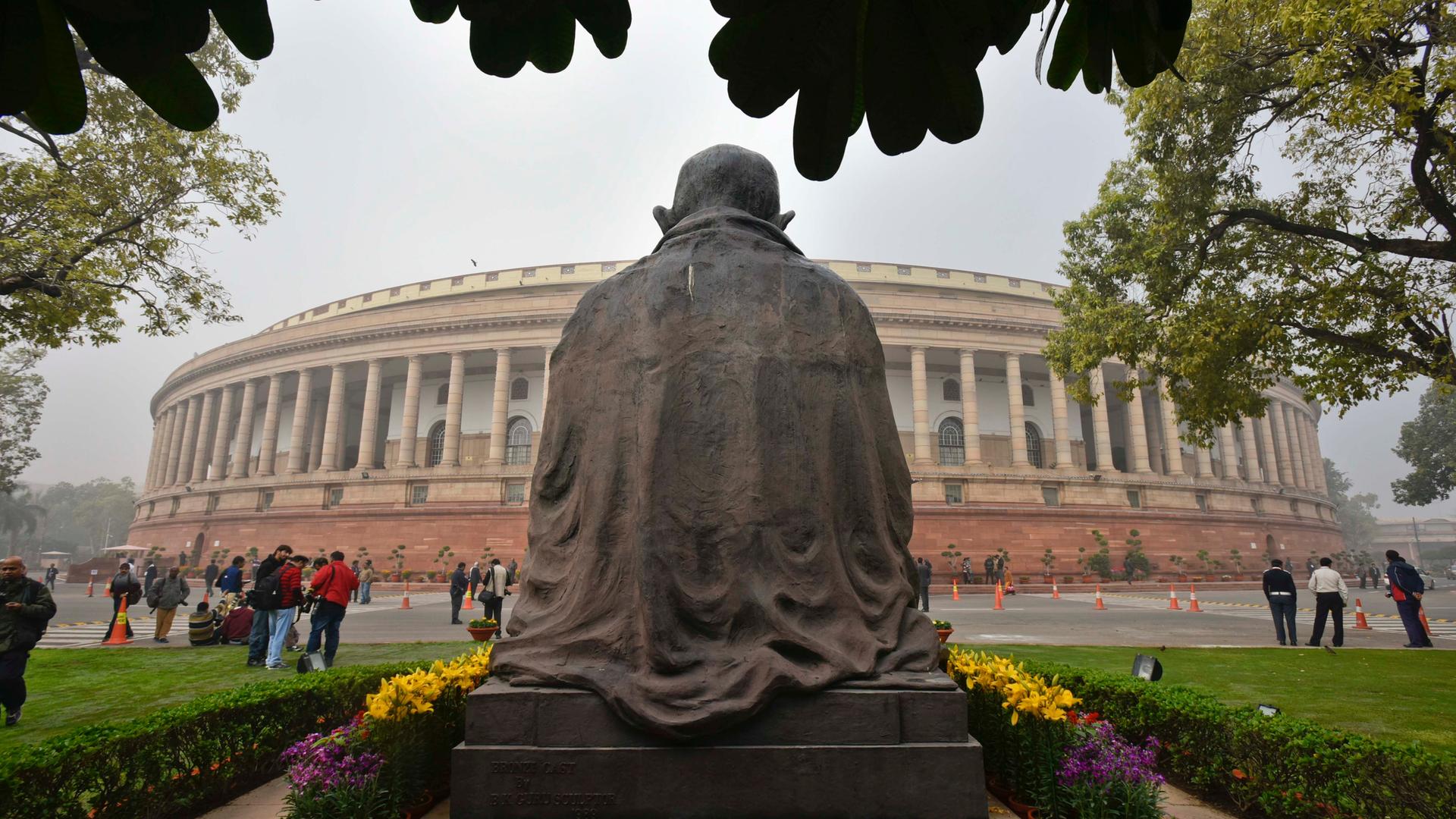 Blick auf das Parlamentsgebäude in Neu-Delhi mit der Rückansicht einer Gandhi-Statue. 