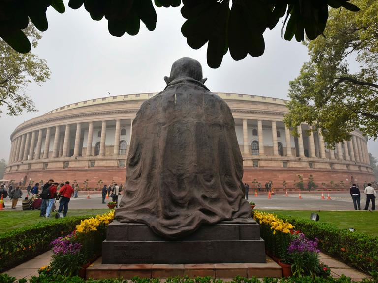 Blick auf das Parlamentsgebäude in Neu-Delhi mit der Rückansicht einer Gandhi-Statue. 