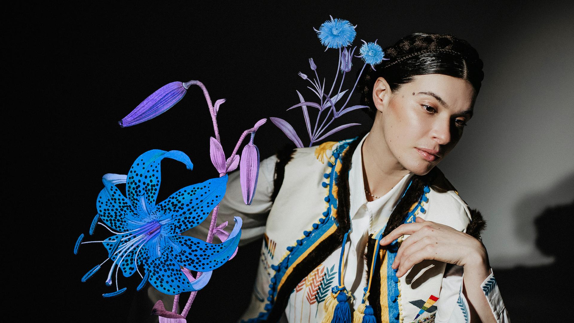 Die ukrainische Sängerin und Musikerin Ganna Grycina ist in ukrainischem Folklore-Oberteil, mit Haarkranz und einer Collage mit einer prächtigen Blume zu sehen. 