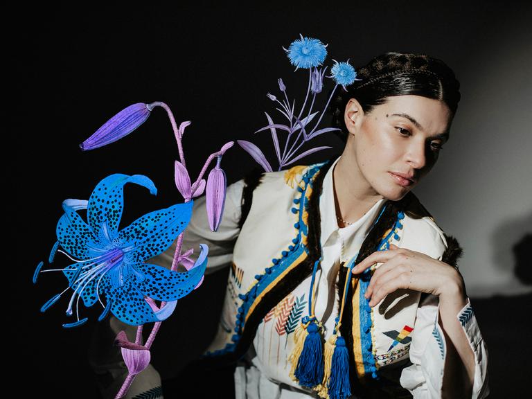 Die ukrainische Sängerin und Musikerin Ganna Grycina ist in ukrainischem Folklore-Oberteil, mit Haarkranz und einer Collage mit einer prächtigen Blume zu sehen. 