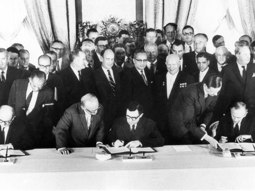 UN-Generalsekretär U Thant (Mitte) und der sowjetische Ministerpräsident Nikita Chruschtschow (r.)  beobachten die Unterzeichnung des Abkommens. Die Unterzeichner von links nach rechts: US-Außenminister Dean Rusk, der sowjetische Außenminister Andrej Gromyko und der britische Außenminister Sir Alec Douglas-Home.