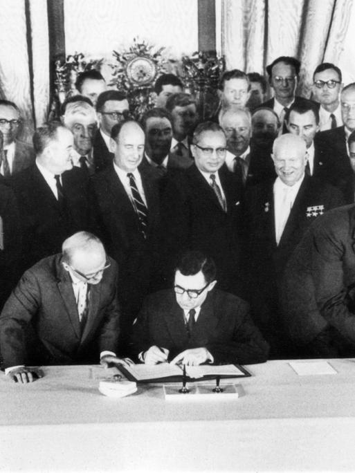UN-Generalsekretär U Thant (Mitte) und der sowjetische Ministerpräsident Nikita Chruschtschow (r.)  beobachten die Unterzeichnung des Abkommens. Die Unterzeichner von links nach rechts: US-Außenminister Dean Rusk, der sowjetische Außenminister Andrej Gromyko und der britische Außenminister Sir Alec Douglas-Home.