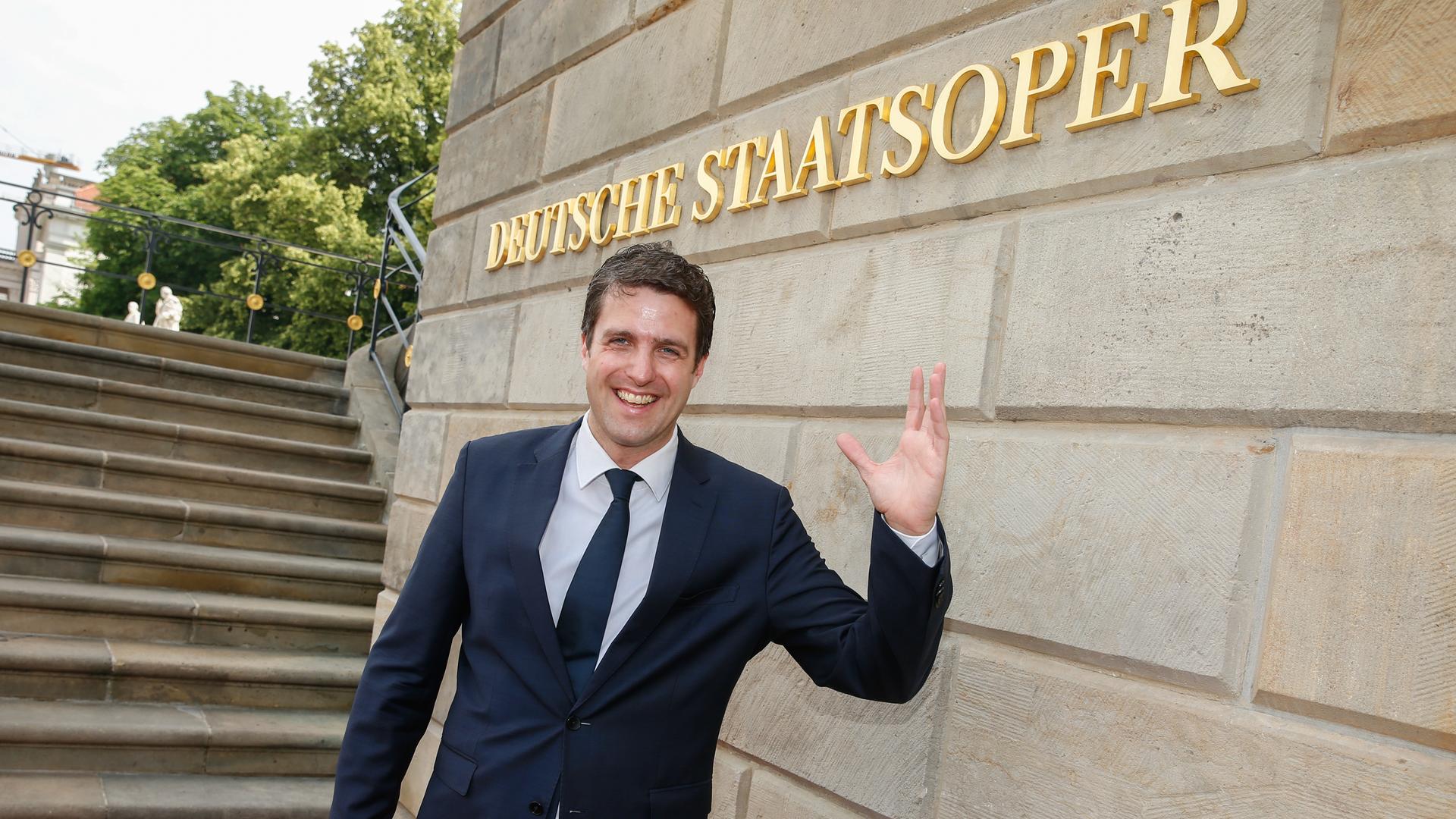 Der Opernintendant Matthias Schulz steht am Eingang der Berliner Staatsoper, hinter ihm an einer Mauer der Schriftzug in goldenen Lettern "Deutsche Staatsoper"