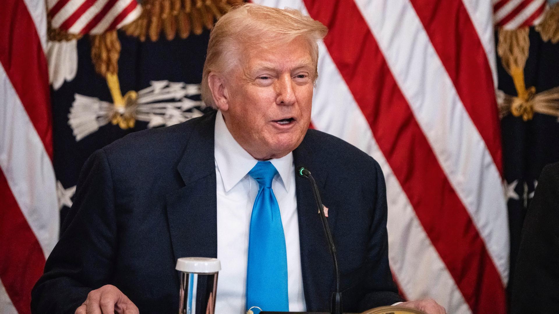 US-Präsident Donald Trump sitzt an einem Schreib-Tisch. Hinter ihm ist die Flagge von dem Land USA. US-Präsident Donald Trump sitzt an einem Schreib-Tisch. Hinter ihm ist die Flagge von dem Land USA.
