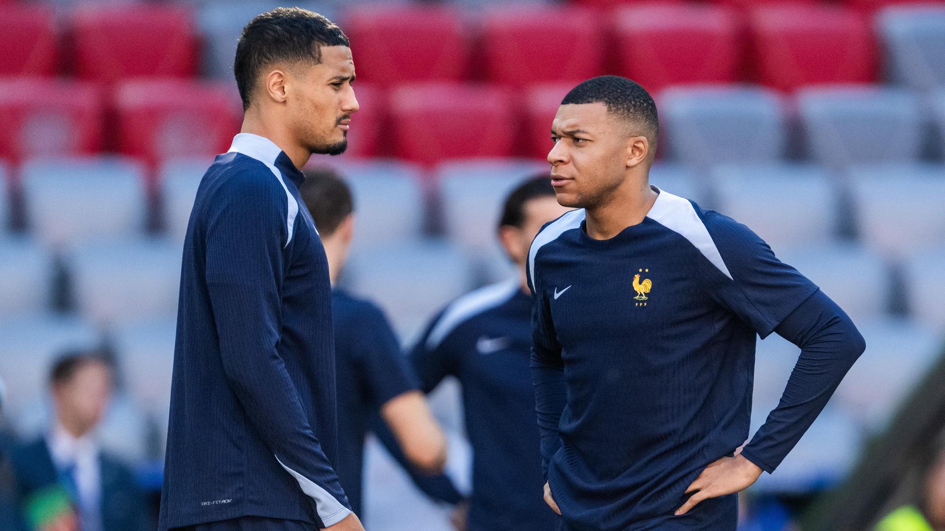 Zu sehen sind die französischen Spieler William Saliba und Kylian Mbappé beim Training im Stadion.