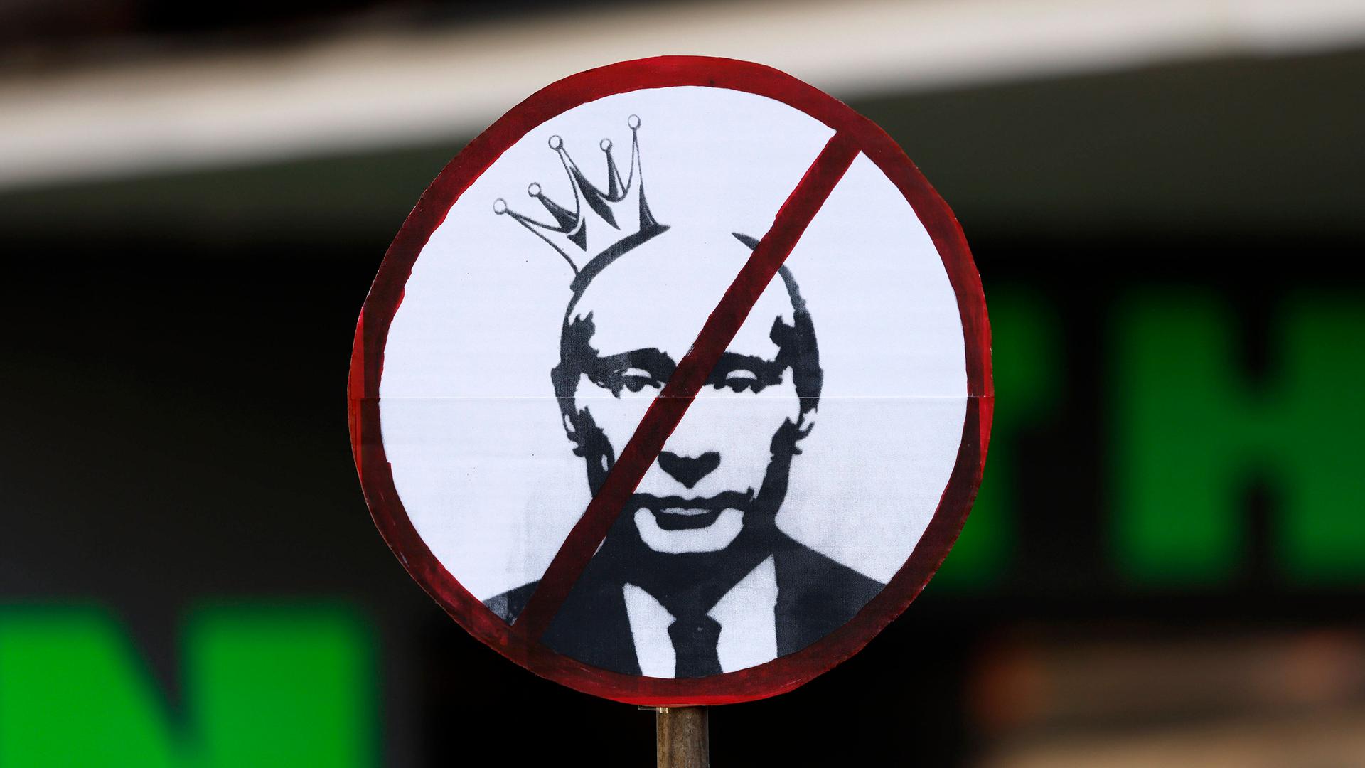 Ein Plakat auf einer Demo zeigt das durchgestrichene Gesicht von Vladimir Putin.