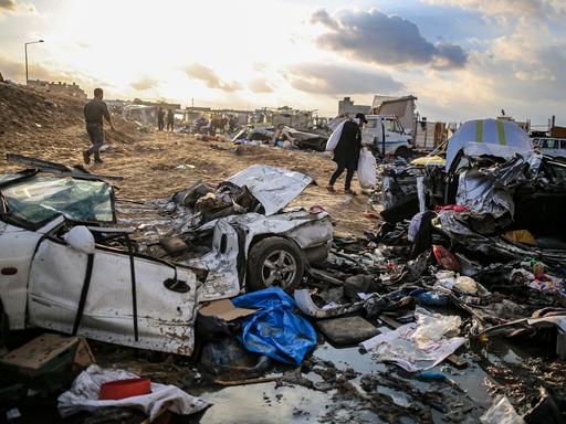 Menschen schultern Säcke in der Nähe von schwer beschädigten Autos, nachdem israelische Panzer das Gebäude des UN-Hilfswerks für Palästinaflüchtlinge in Khan Yunis, Gaza, am 26. Januar 2024 beschossen haben. Durch den Panzerbeschuss der israelischen Armee wurden das Gebäude und seine Umgebung schwer beschädigt.