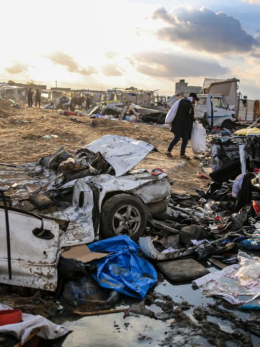 Menschen schultern Säcke in der Nähe von schwer beschädigten Autos, nachdem israelische Panzer das Gebäude des UN-Hilfswerks für Palästinaflüchtlinge in Khan Yunis, Gaza, am 26. Januar 2024 beschossen haben. Durch den Panzerbeschuss der israelischen Armee wurden das Gebäude und seine Umgebung schwer beschädigt.