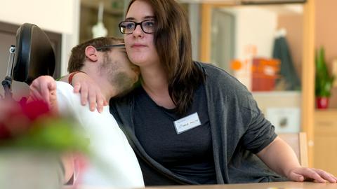 Freiwilliges Soziales Jahr: Eine junge Frau kümmert sich in einem Wohnheim der Diakonie um einen behinderten jungen Mann. Dieser legt vertrauensvoll sein Gesicht an ihre Schulter.
