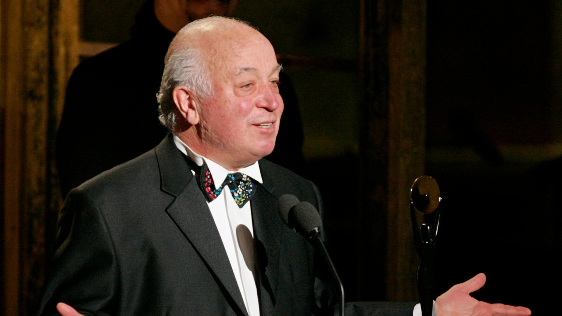 Der Musikproduzent Seymour Stein sitzt auf einem roten Sofa