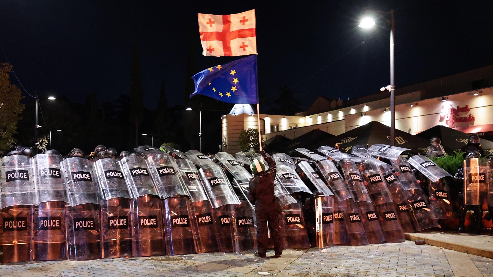 Ein Demonstrant schwenkt vor Polizisten eine georgische und eine EU-Flagge.