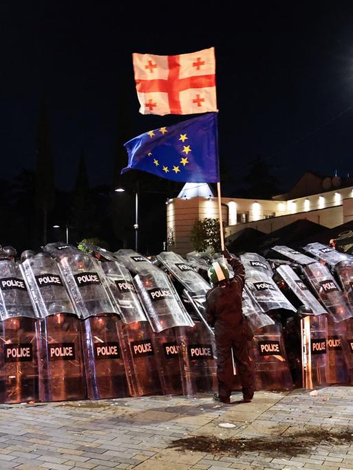 Ein Demonstrant schwenkt vor Polizisten eine georgische und eine EU-Flagge.
