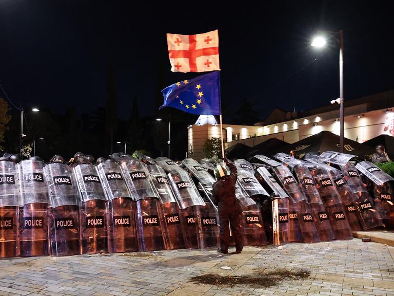 Ein Demonstrant schwenkt vor Polizisten eine georgische und eine EU-Flagge.