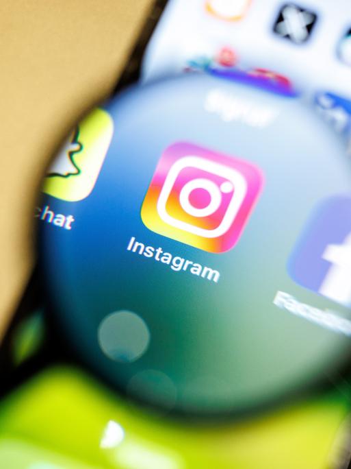 Das Logo der App Instagram ist am 29.12.2024 durch eine Lupe auf dem Display von einem Smartphone zu sehen. Instagram ist ein soziales Netzwerk mit Fokus auf Video- und Foto-Sharing, das vom Unternehmen Meta Platforms betrieben wird.