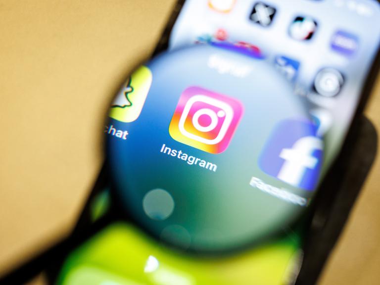 Das Logo der App Instagram ist am 29.12.2024 durch eine Lupe auf dem Display von einem Smartphone zu sehen. Instagram ist ein soziales Netzwerk mit Fokus auf Video- und Foto-Sharing, das vom Unternehmen Meta Platforms betrieben wird.