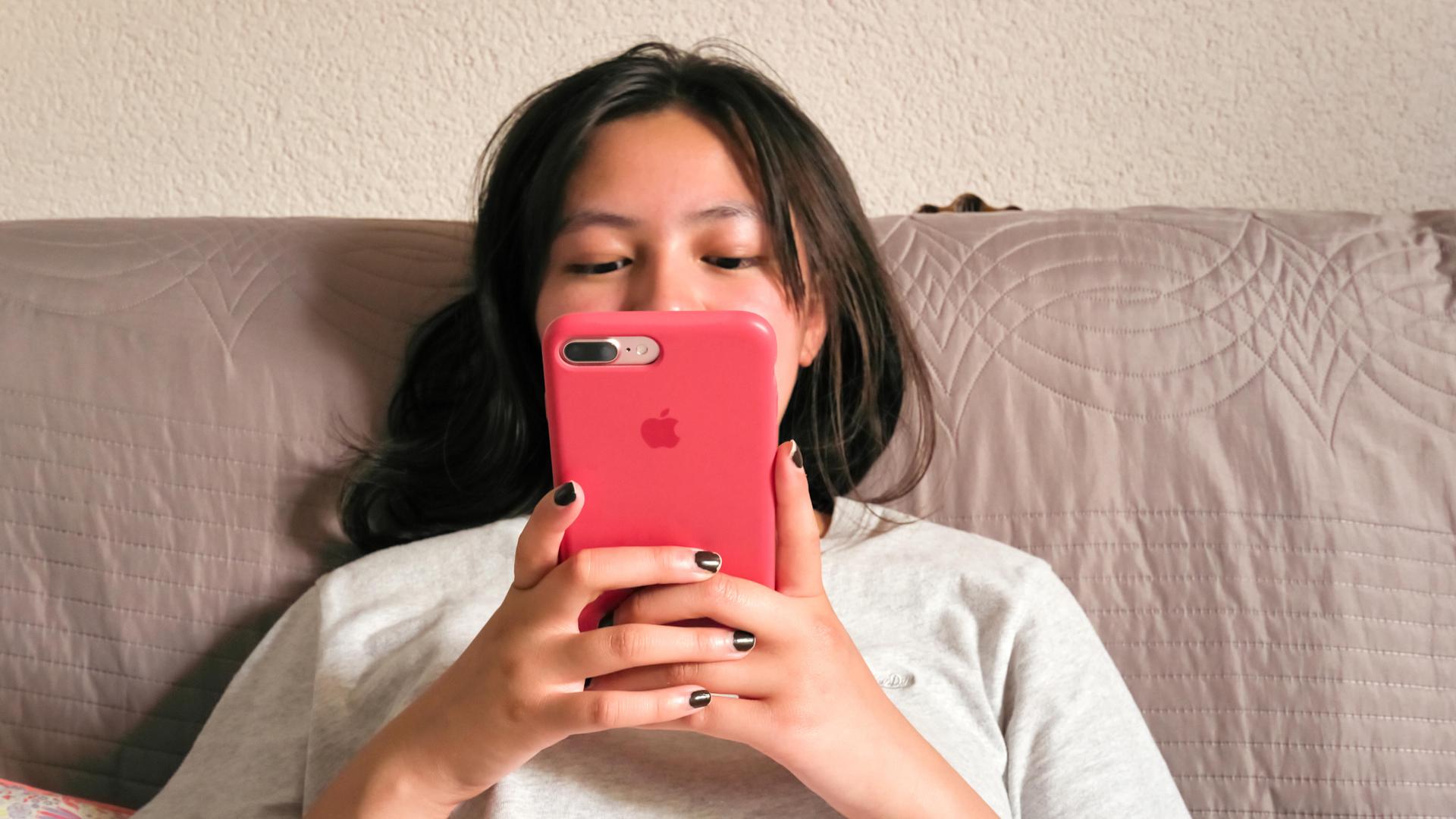 Eine Teenagerin sitzt mit Smartphone auf dem Sofa.