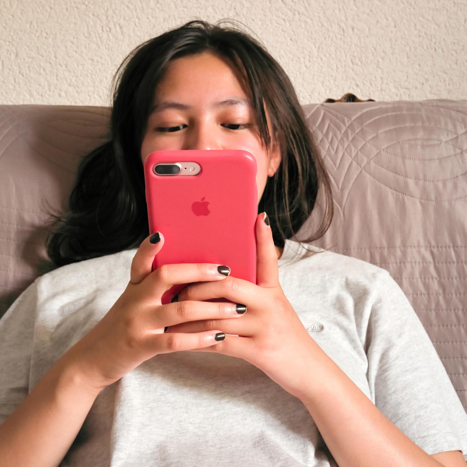 Eine Teenagerin sitzt mit Smartphone auf dem Sofa.