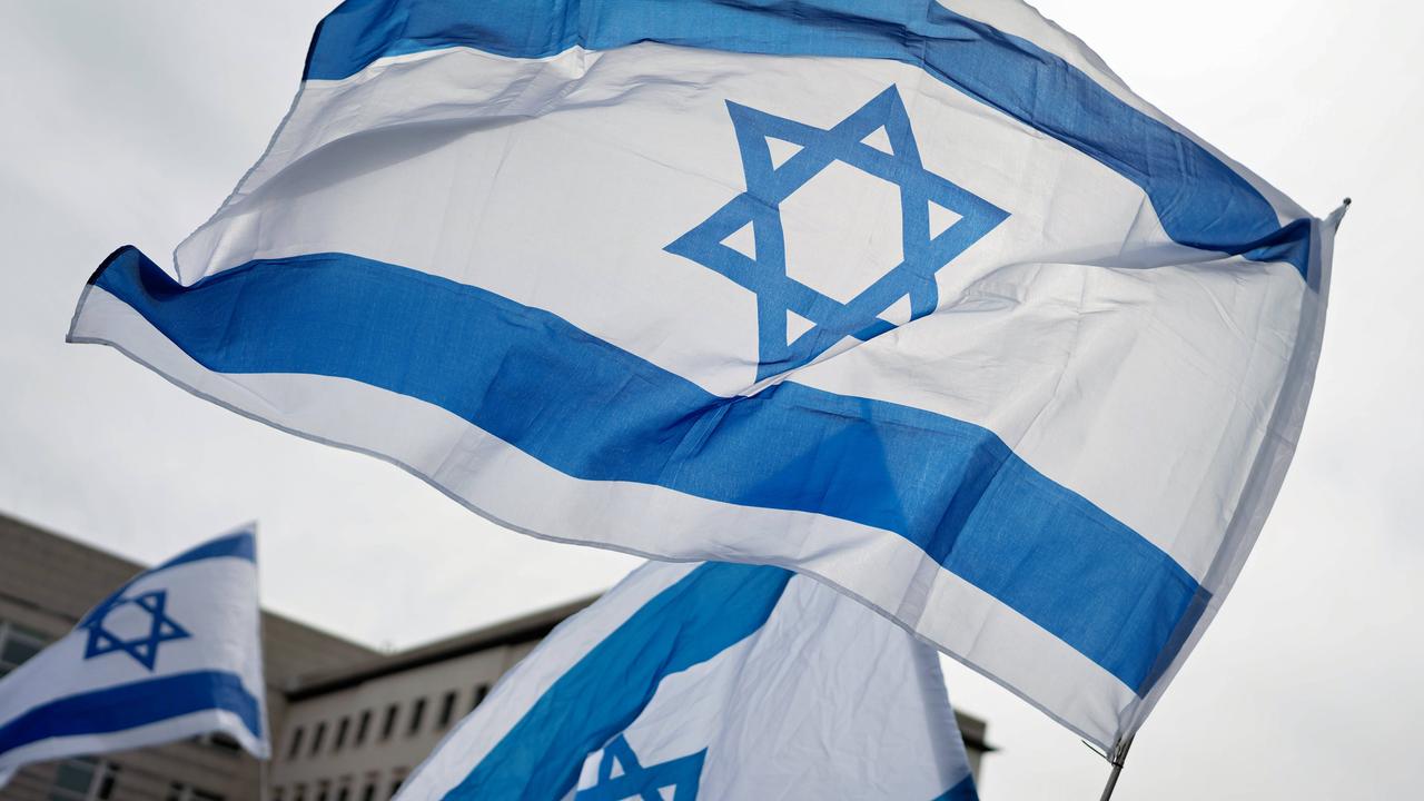 Eine große und zwei kleinere Israel-Flaggen wehen vor einem bedecken Himmel.