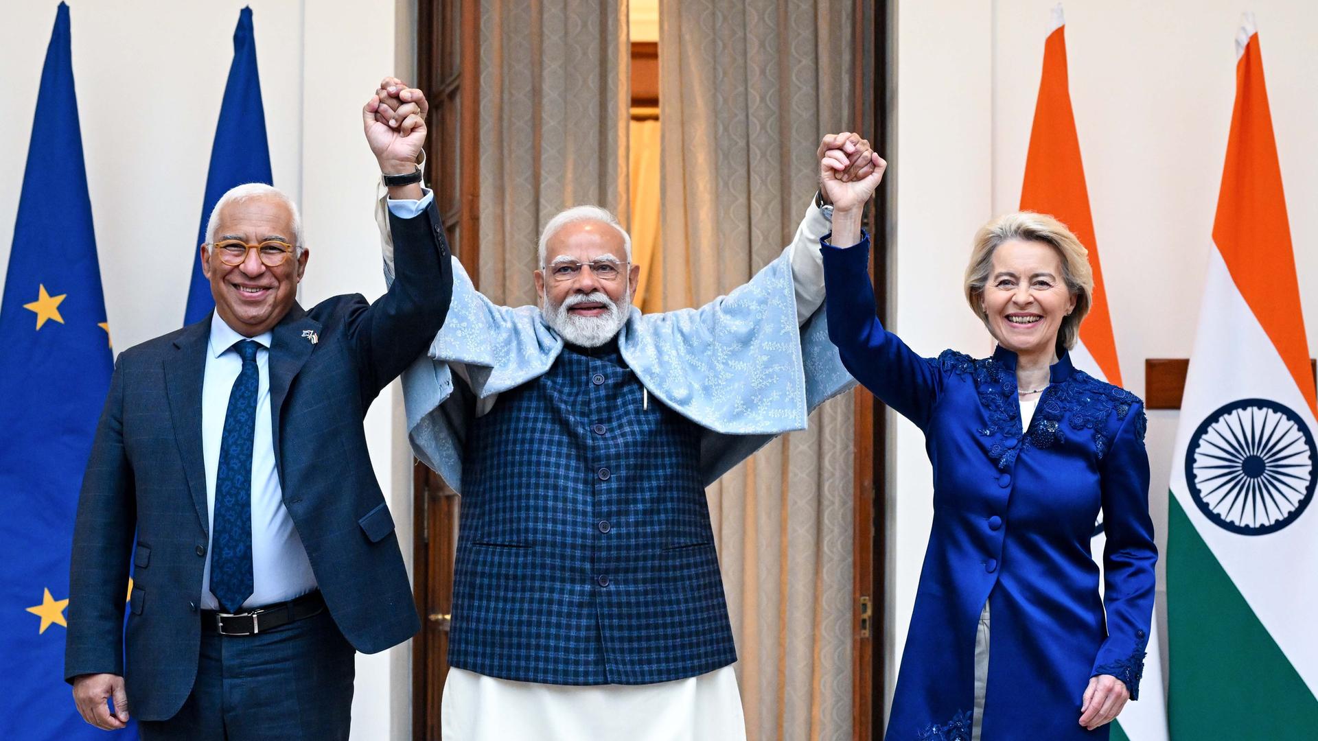 EU-Ratspräsident Antonio Costa (l.), Indiens Premierminister Narendra Modi (Mitte) und EU-Kommissionspräsidentin Ursula von der Leyen (r.) stehen mit nach oben gestreckten Armen nebeneinander. Sie feiern das Handelsabkommen zwischen der EU und Indien.