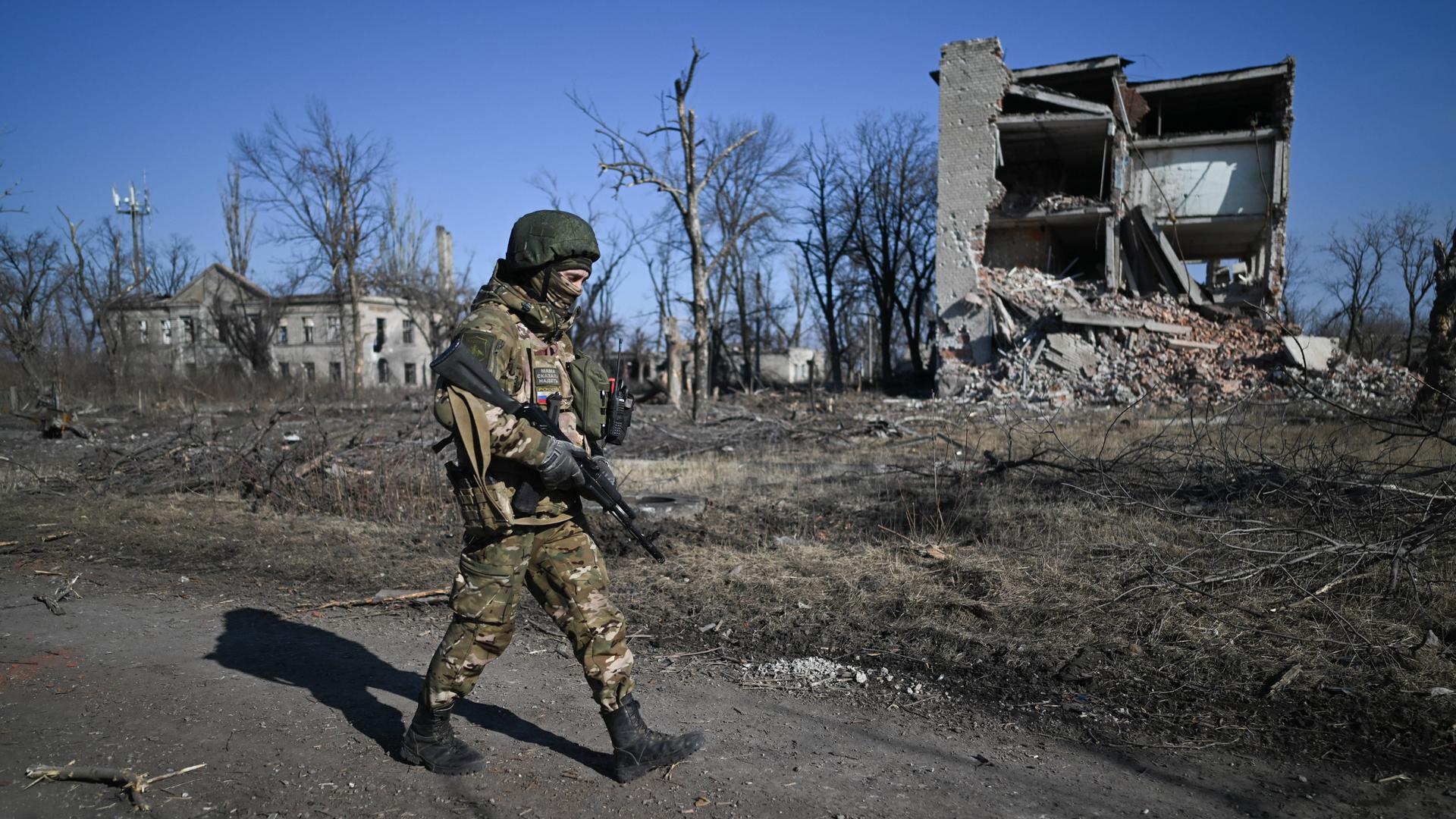 Ein russischer Soldat läuft durch Awdijiwka in der Ukraine. Im Hintergrund kahle Bäume und ein zerstörtes Haus.