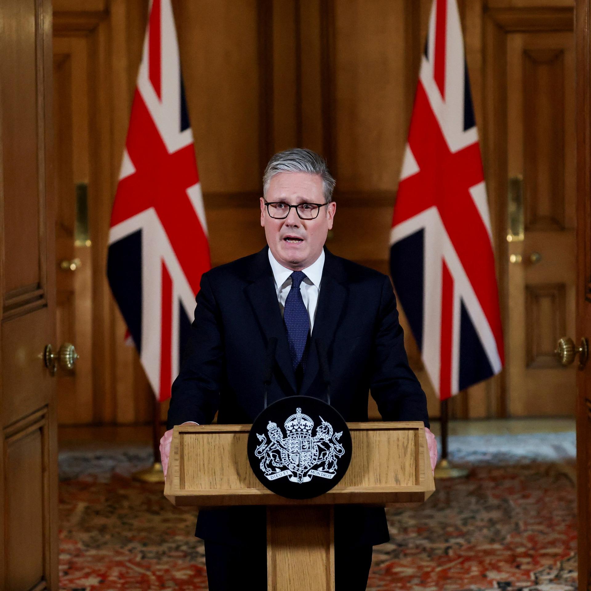 Der britische Premierminister Starmer steht hinter einem Rednerpult, hinter ihm zwei Landesflaggen.