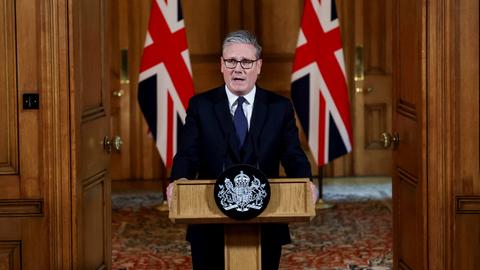 Der britische Premierminister Starmer steht hinter einem Rednerpult, hinter ihm zwei Landesflaggen.