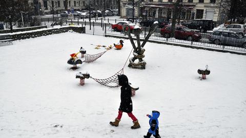 Eine Mutter mit ihrem Kind geht allein über einen verschneiter Spielplatz am Kollwitzplatz im Ortsteil Prenzlauer Berg in Berlin.