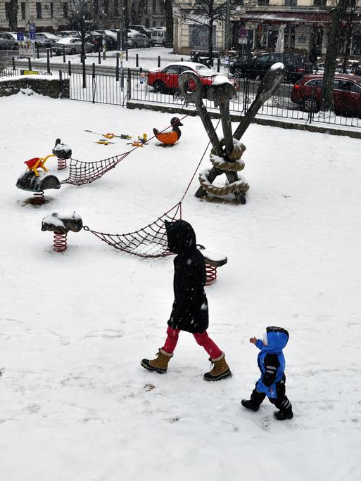 Eine Mutter mit ihrem Kind geht allein über einen verschneiter Spielplatz am Kollwitzplatz im Ortsteil Prenzlauer Berg in Berlin.