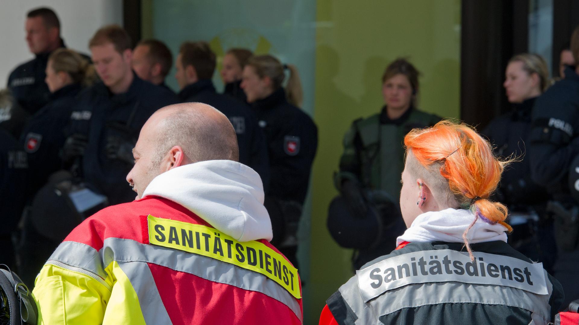 Sanitäter und Polizisten stehen zusammen, die Sanitäter sind im Vordergrund von hinten zu sehen, die Polizisten verschwommen im Hintergrund Sanitäter und Polizisten stehen zusammen, die Sanitäter sind im Vordergrund von hinten zu sehen, die Polizisten verschwommen im Hintergrund