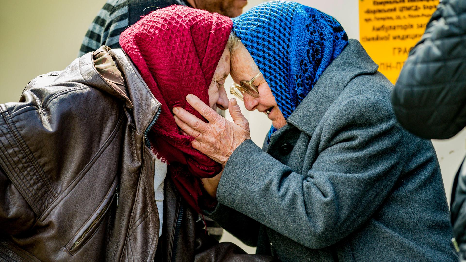 Zwei alte Frauen mit Kopftuch umarmen sich. 