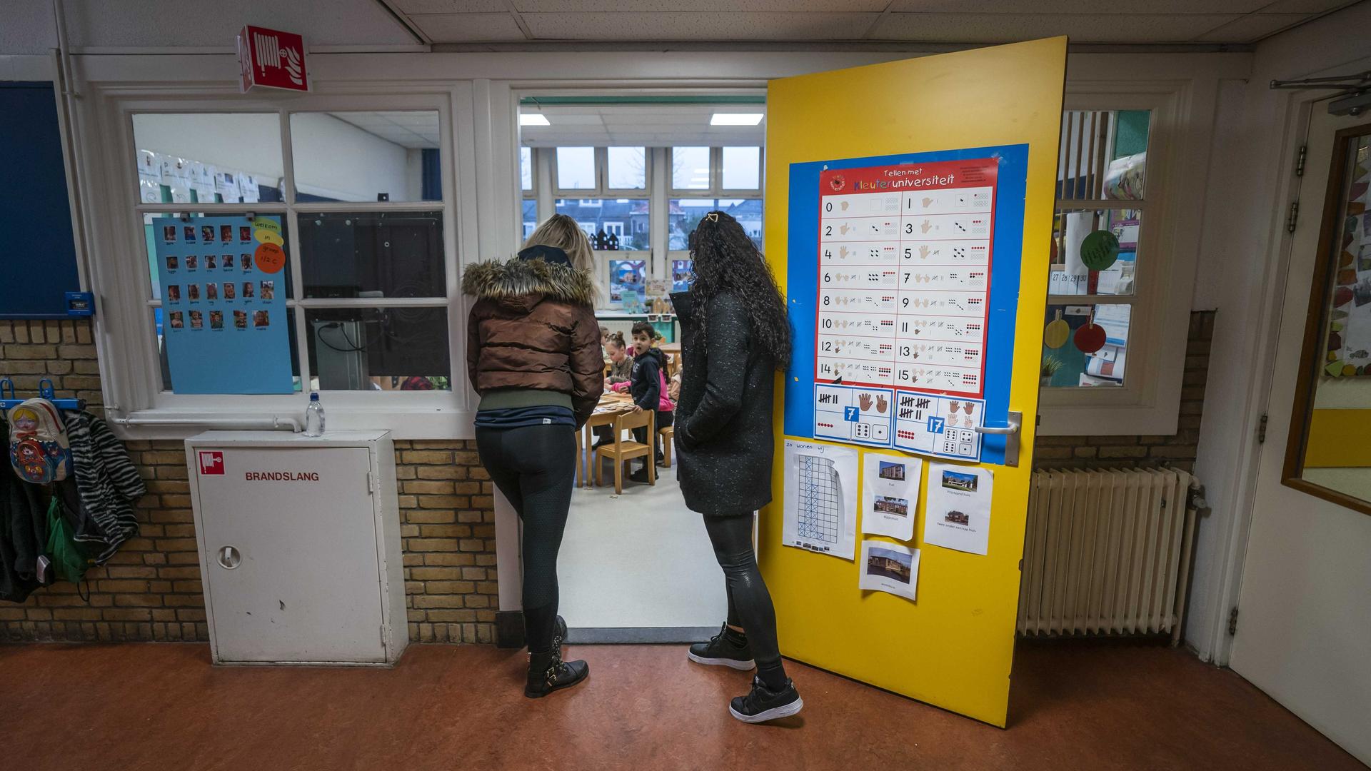 Zwei Frauen stehen in der offenen Eingangstür eines Klassenraums und schauen hinein zu den Grundschülern.