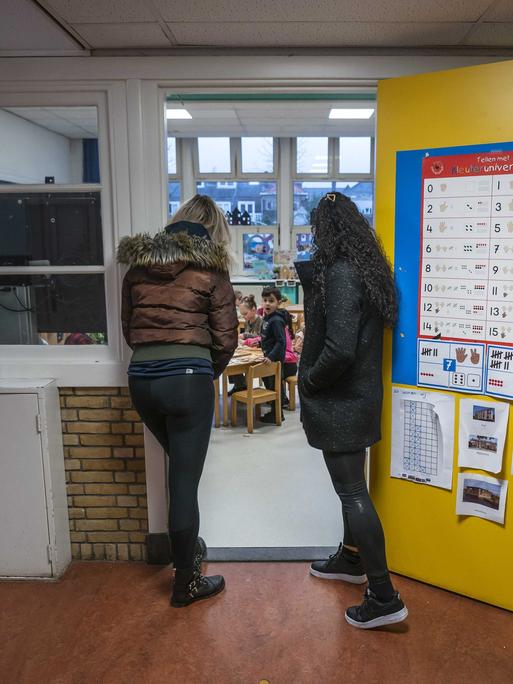 Zwei Frauen stehen in der offenen Eingangstür eines Klassenraums und schauen hinein zu den Grundschülern.