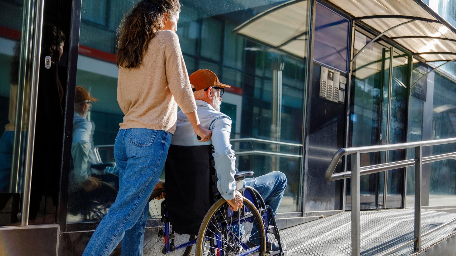 Pflegekraft schiebt älteren Mann im Rollstuhl eine Rampe hinauf