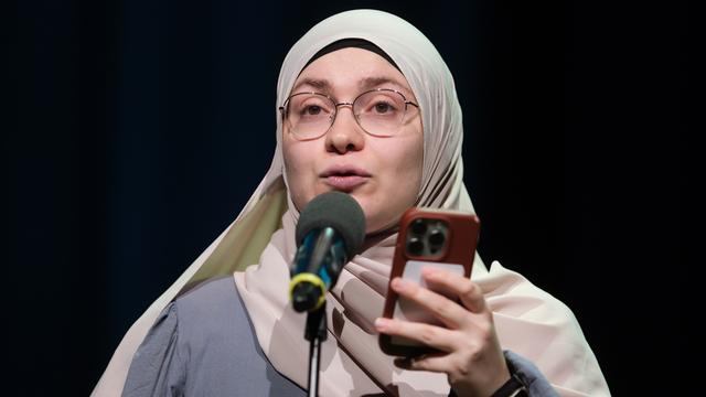 Ayse Irem steht hinter einem Mikrofon. Sie liest einen Text von ihrem Mobil-Telefon ab. 