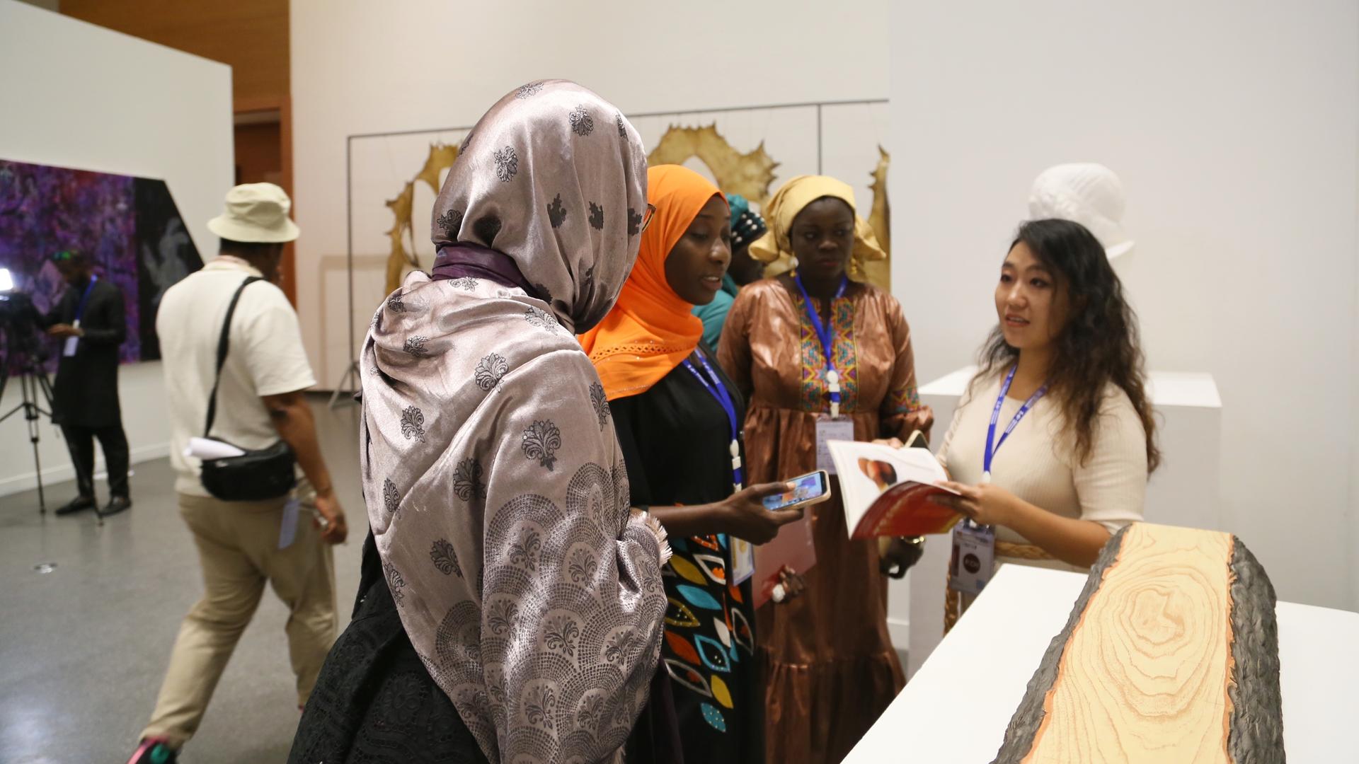 Eine chinesische Ausstellerin stellt den Besucherinnen im China-Pavillon der Dakar-Biennale für zeitgenössische afrikanische Kunst 2022 in Dakar ihre Werke vor. Sie hält eine