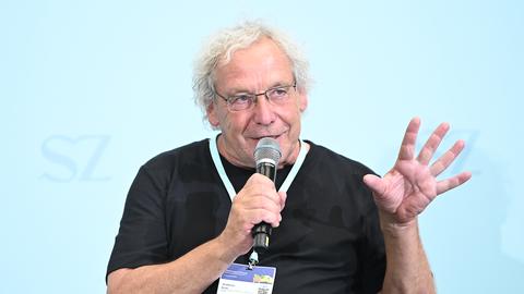 Der Soziologe und Verkehrsforscher Andreas Knie auf dem Nachhaltigkeitsgipfel 2025 bei einer Diskussion. Er trägt ein schwarzes T-Shirt, eine Brille und hat ein Mikrofon in der rechten Hand, in das er hinein spricht.