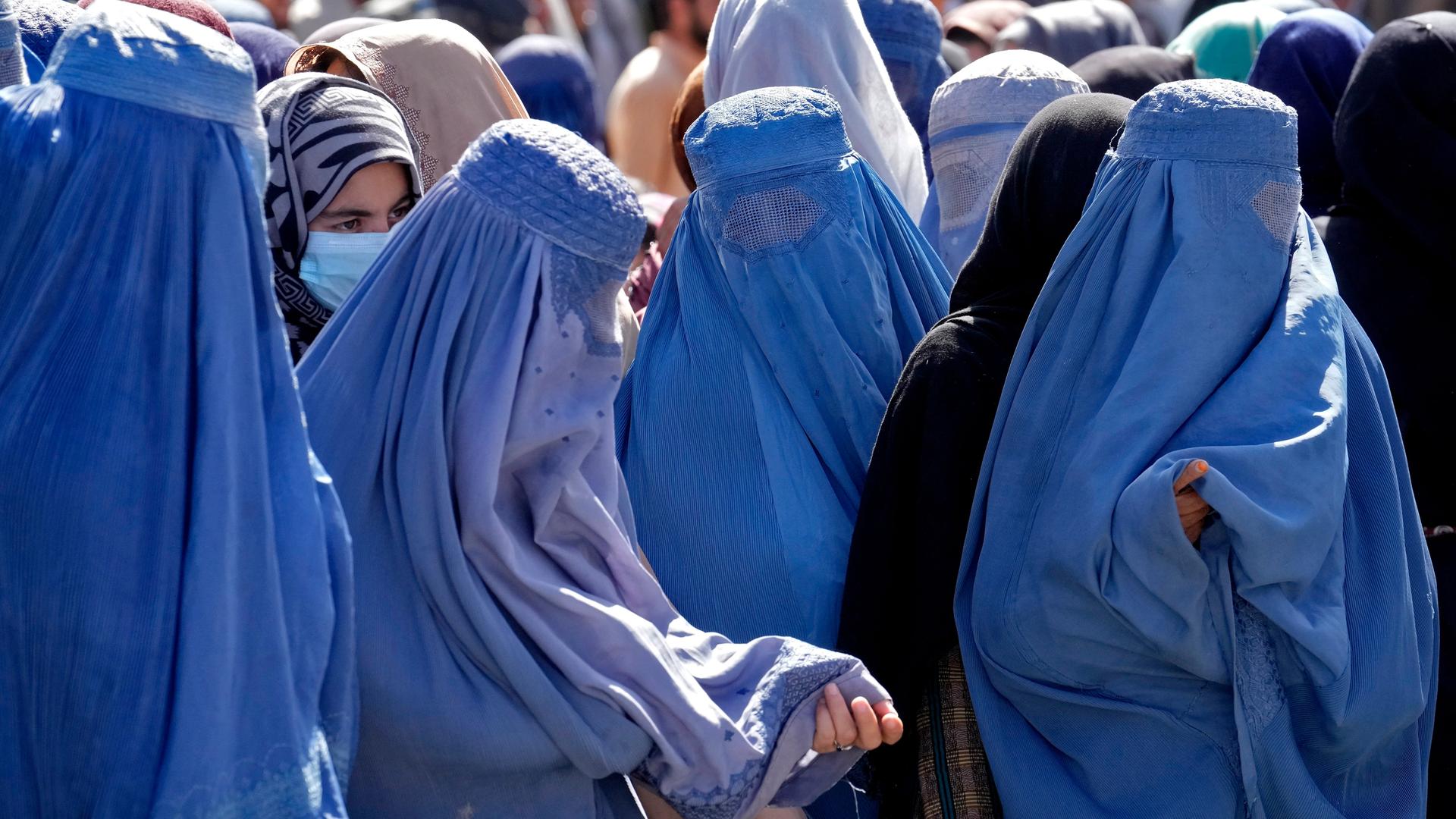 Frauen in blauen Burkas stehen in einer Schlange.