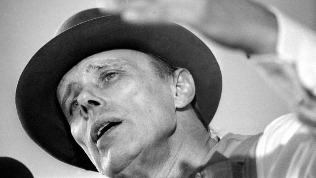 Der Künstler Joseph Beuys in Untersicht auf einem Schwarz-Weiß-Foto. Er diskutiert.