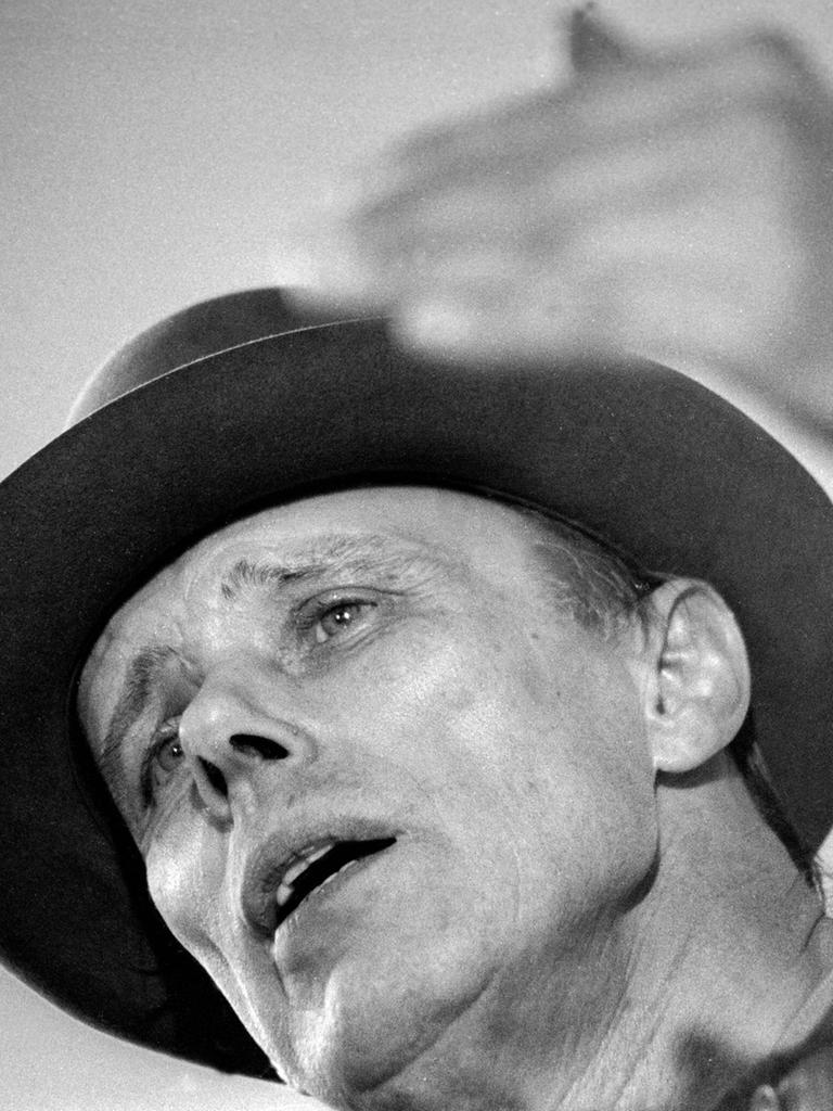 Der Künstler Joseph Beuys in Untersicht auf einem Schwarz-Weiß-Foto. Er diskutiert.