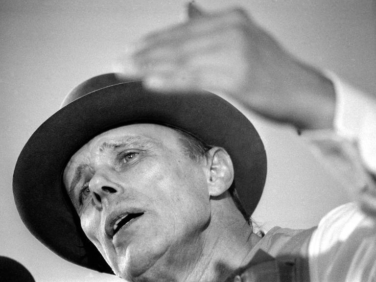 Der Künstler Joseph Beuys in Untersicht auf einem Schwarz-Weiß-Foto. Er diskutiert.