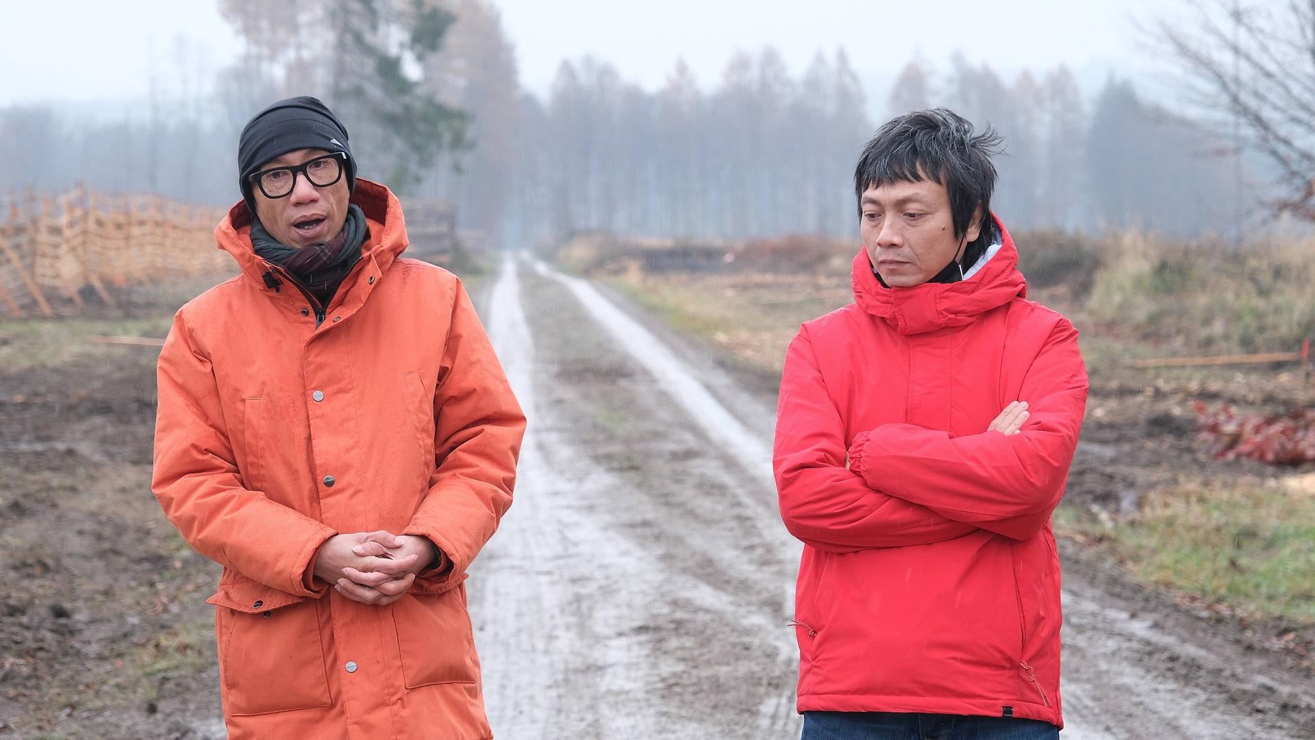 Iswanto Hartono und Reza Afisina von der Künstlergruppe Ruangrupa tragen orange Anoraks, hinter ihnen ist ein Forstweg zu sehen.