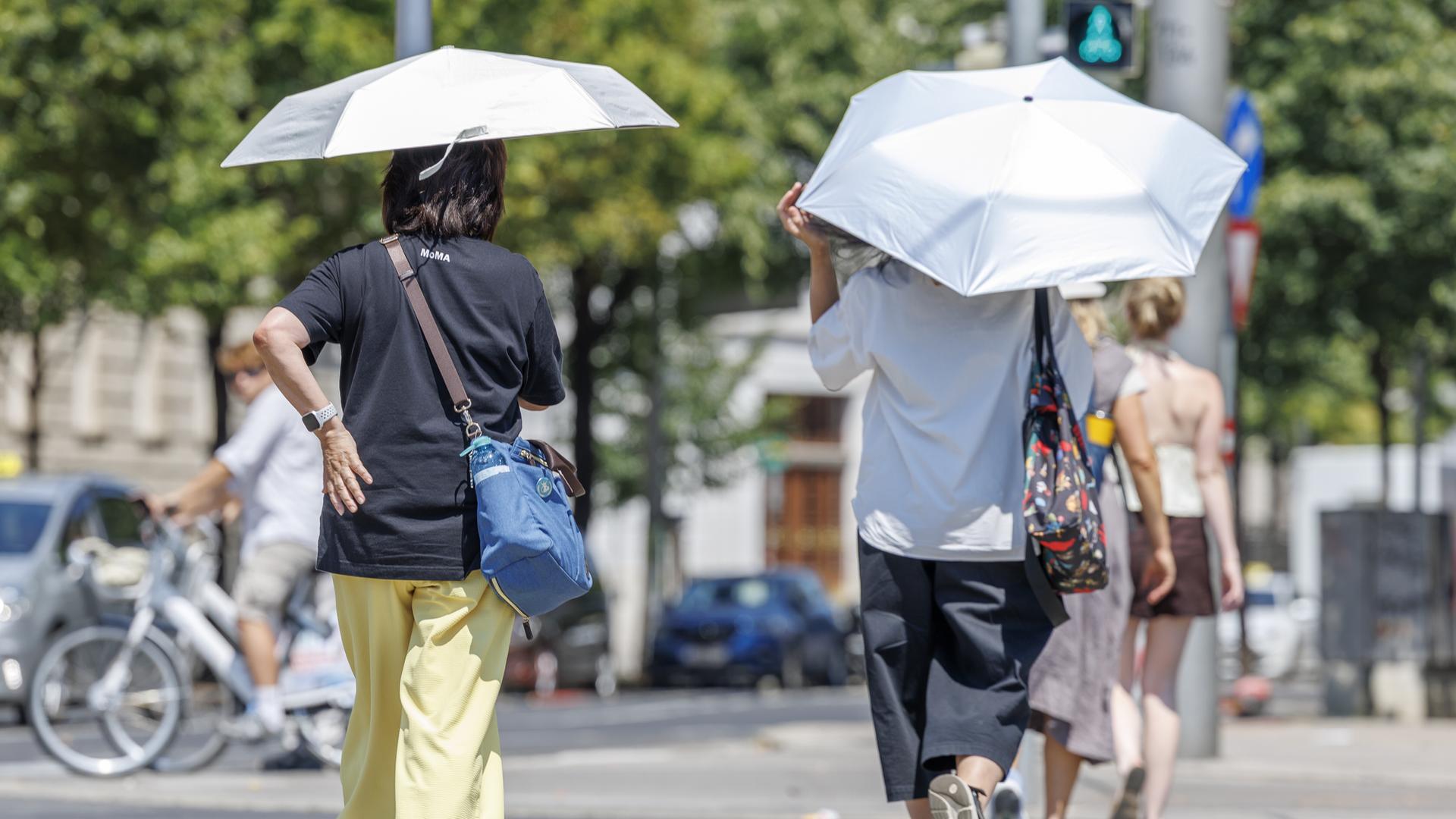 Zwei Fußgängerinnen in der Stadt halten Regenschirme über den Kopf, um sich vor der Sonne zu schützen.
