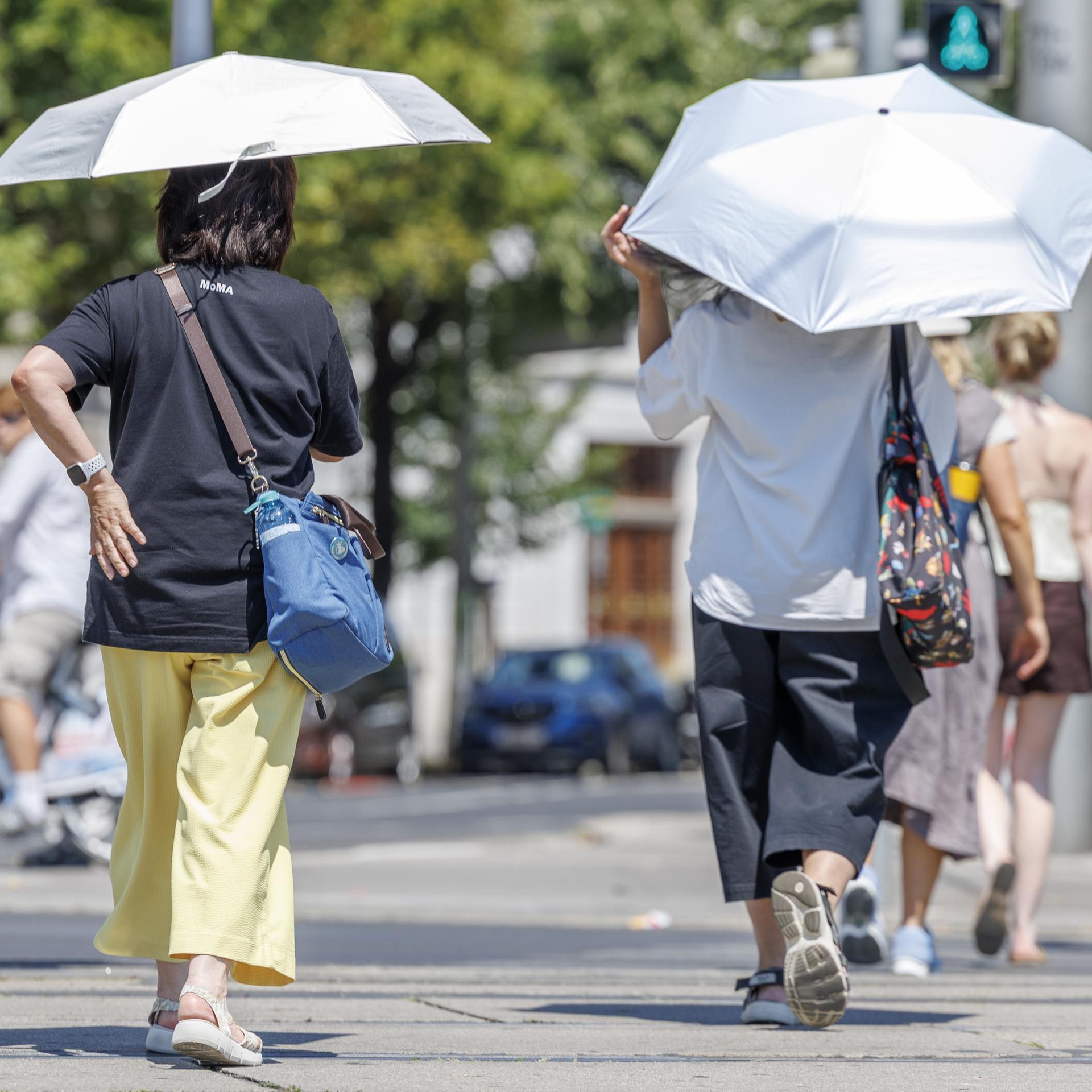 Zwei Fußgängerinnen in der Stadt halten Regenschirme über den Kopf, um sich vor der Sonne zu schützen.