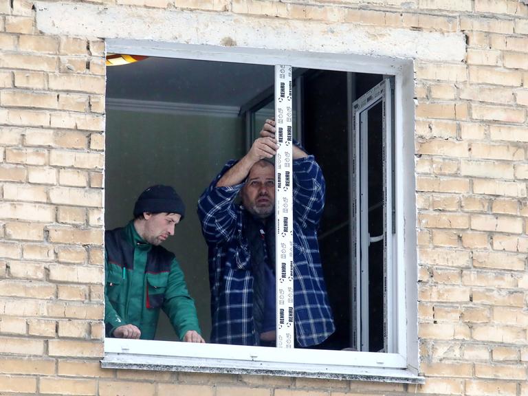Zwei Männer reparieren ein kaputtes Fenster nach einem russischen Luftangriff in der Ukraine.  