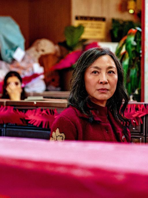 Michelle Yeoh blickt ernst über die Kante eines roten Sofas