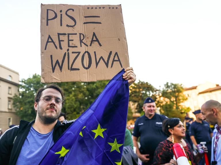 Ein Demonstrant hält in Krakau ein Banner hoch auf dem er gegen die Visa-Affäre protestiert sowie die Europafahne.  