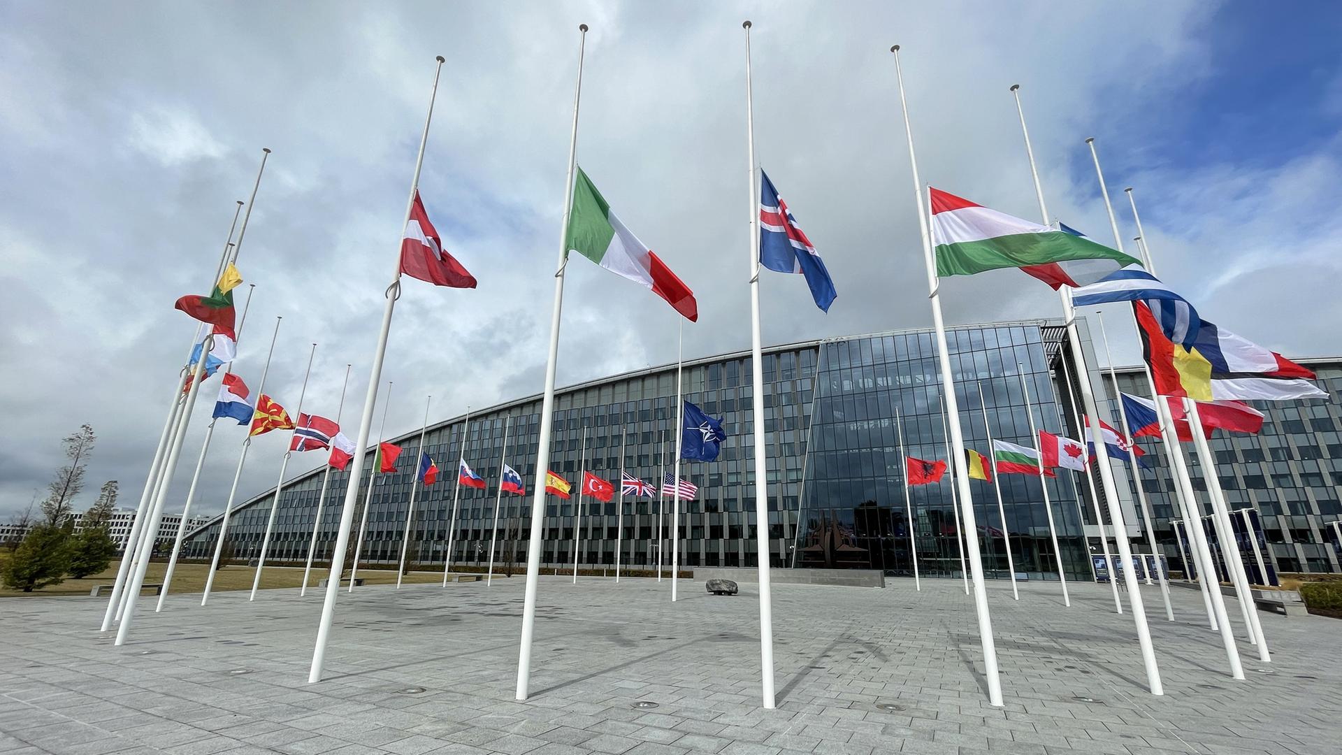 Flaggen wehen vor dem Nato-Hauptquartier, einem Gebäude mit Glasfassade. 