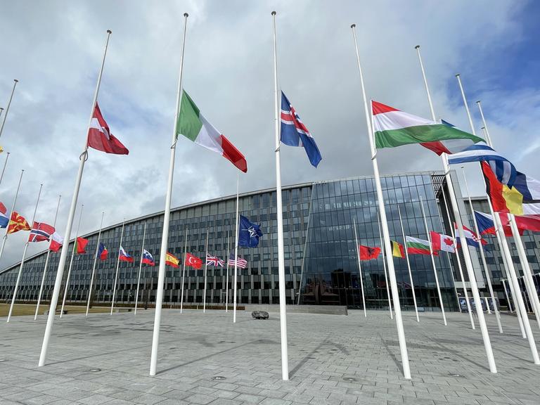 Flaggen wehen vor dem Nato-Hauptquartier, einem Gebäude mit Glasfassade. 