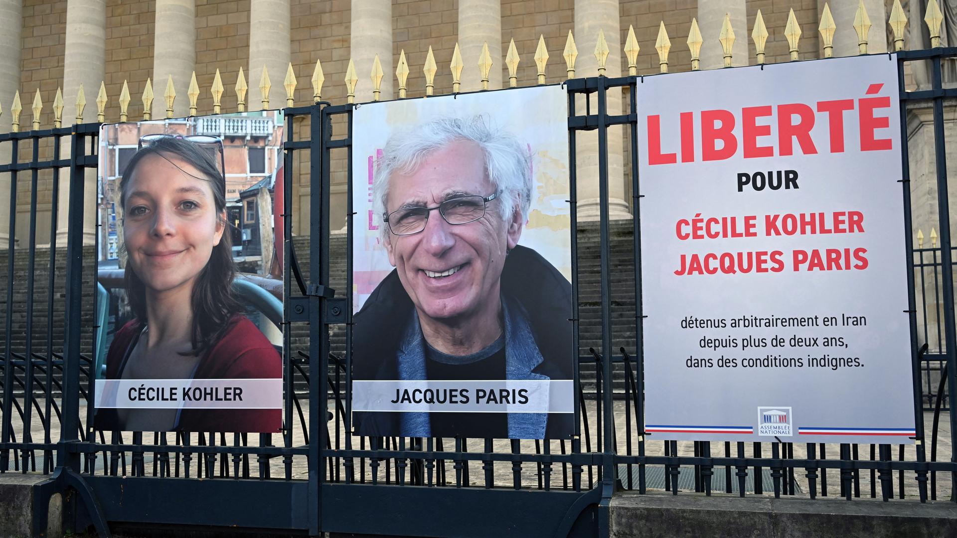 An einem Zaun hängen Plakate mit den Gesichtern der beiden im Iran ihaftierten Franzosen am Rande einer Demonstration.