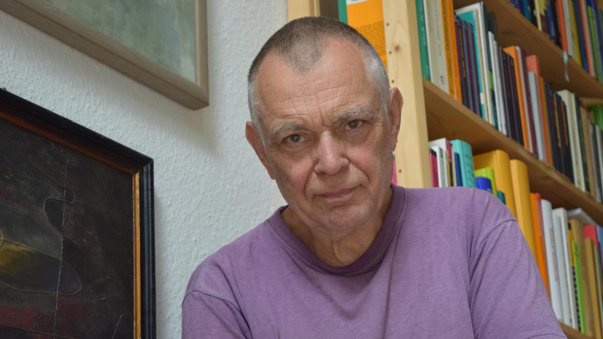 Der Komponist Mathias Spahlinger sitzt auf einer Treppe vor Bücherregalen und schaut in die Kamera